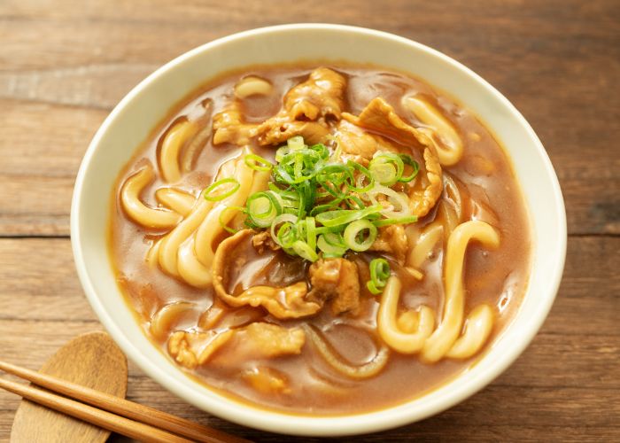 A bowl of curry udon, showing udon noodles and meat in a cozy bowl of curry soup.